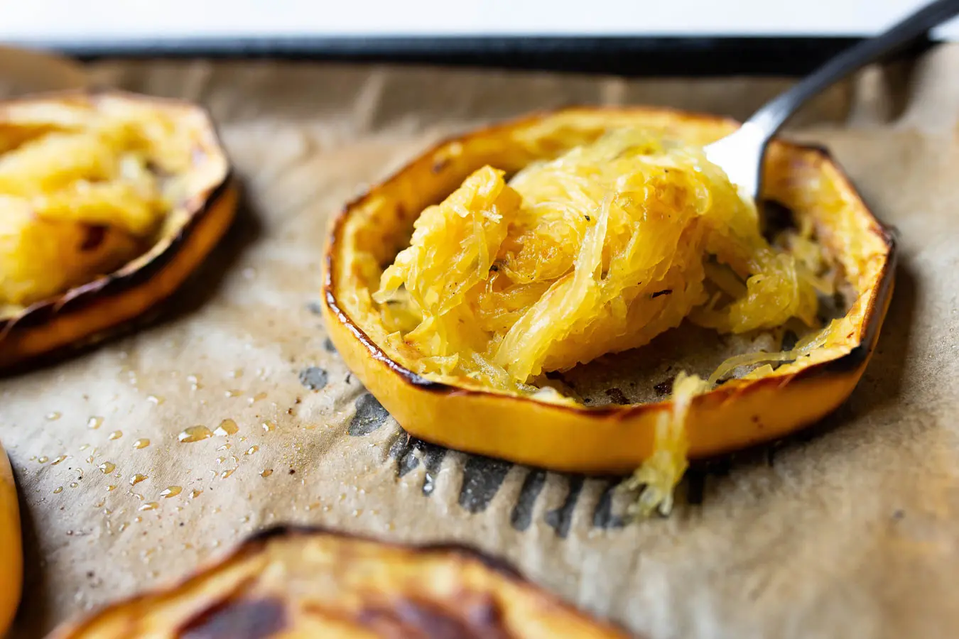 Roasted Spaghetti Squash rings on a lined baking tray. A fork has been used to gather all the spaghetti strands from the inside of the ring, leaving the skin intact.