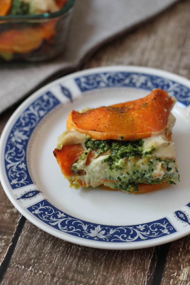 A portion of Vegan Butternut Squash Lasagna on a white plate with a blue trim. That lasagna n has lots of layers and is topped with orange butternut squash. You can see the white vegan cheese sauce as well as the green kale pesto.