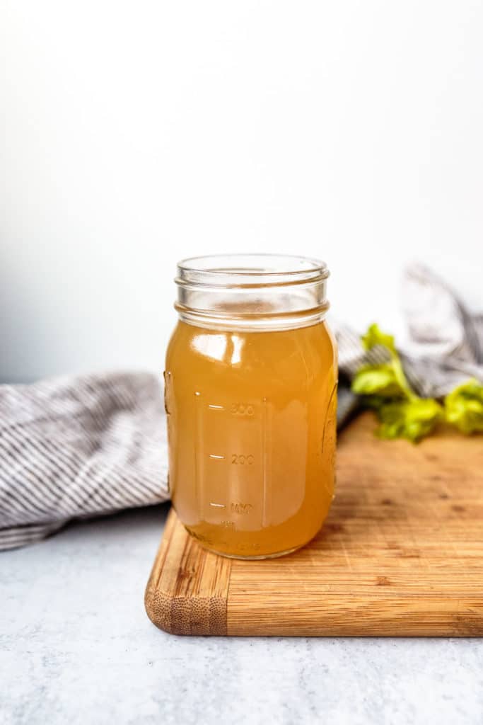 bone broth in a mason jar with a cutting board, kitchen towel, and herbs