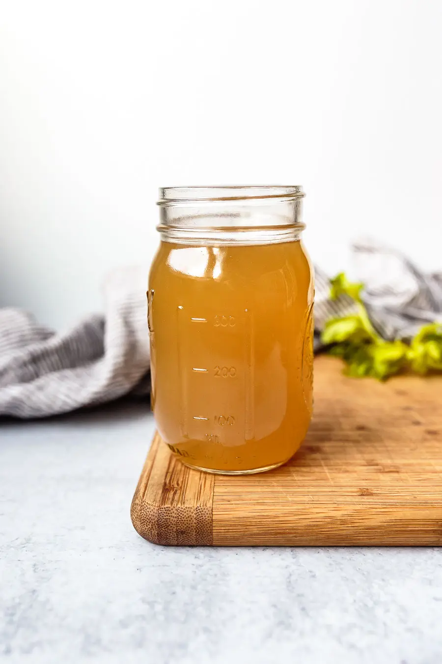 Side view of a mason jar with no lid on, filled with slow cooker bone broth. It is sitting on a wooden cutting board.
