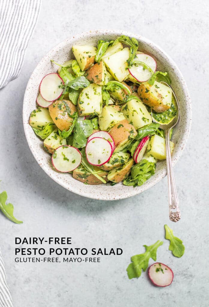 Potato salad with arugula, pesto and radishes in a white bowl.