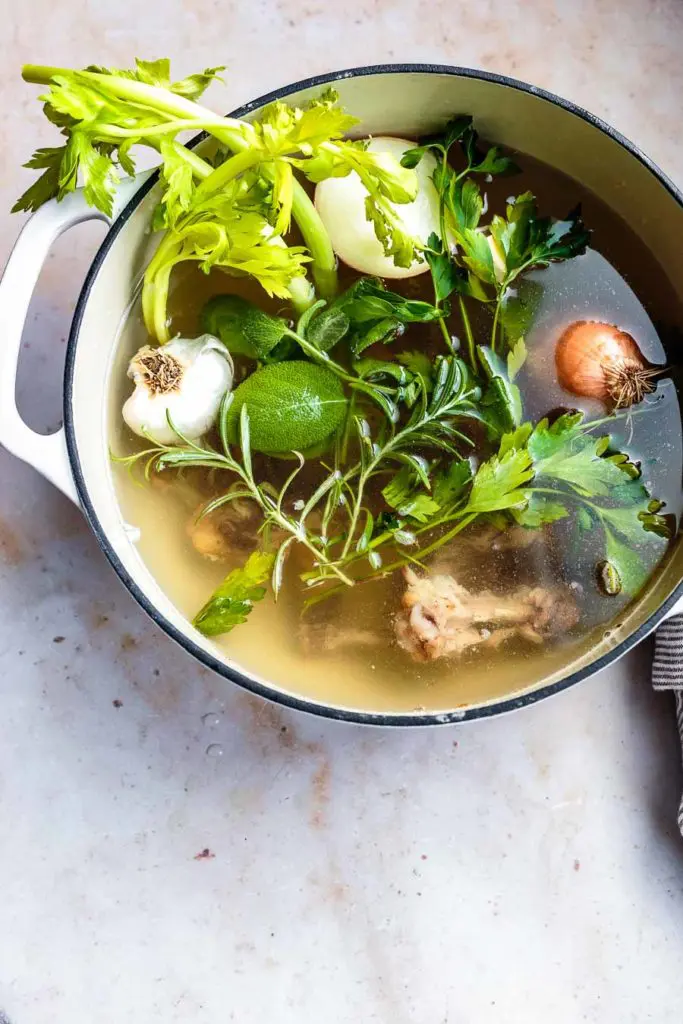 bone broth with herbs and aromatics in a dutch oven