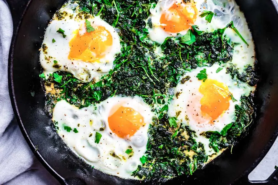 Close up, view from above of green shakshuka in a black skillet. The veggies are green and wilted and the eggs are poached and bright.