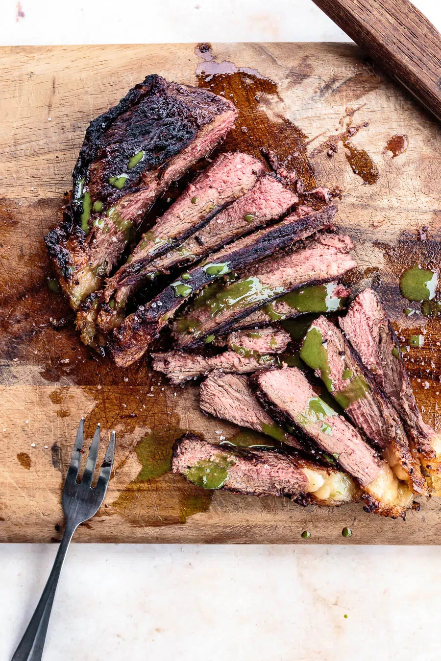 Grilled picanha steak on a cutting board. It is sliced and drizzled in chimichurri sauce.