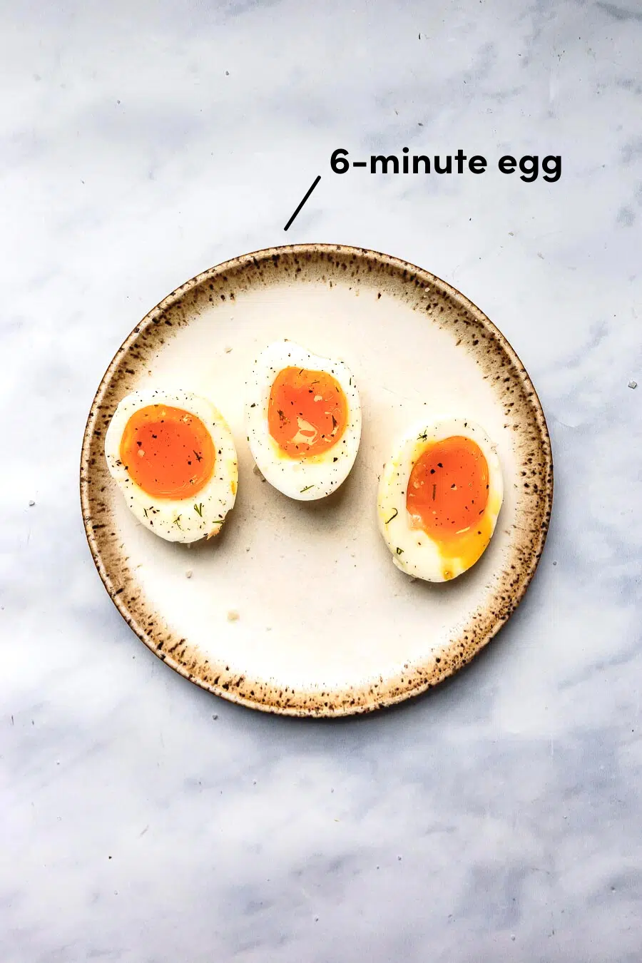 three jammy boiled eggs halved and resting on a stoneware place topped with salt and pepper and 6-minute cook time indicator