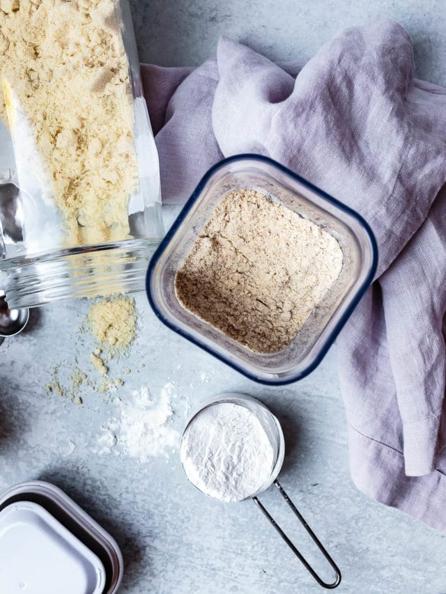 overhead view of gluten-free flours in glass jars with measuring cups coconut flour tigernut flour and almond flour