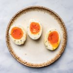 three jammy boiled eggs halved and resting on a stoneware place topped with salt and pepper