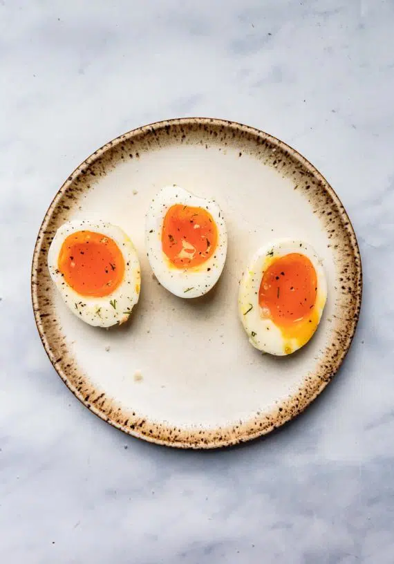 three jammy boiled eggs halved and resting on a stoneware place topped with salt and pepper