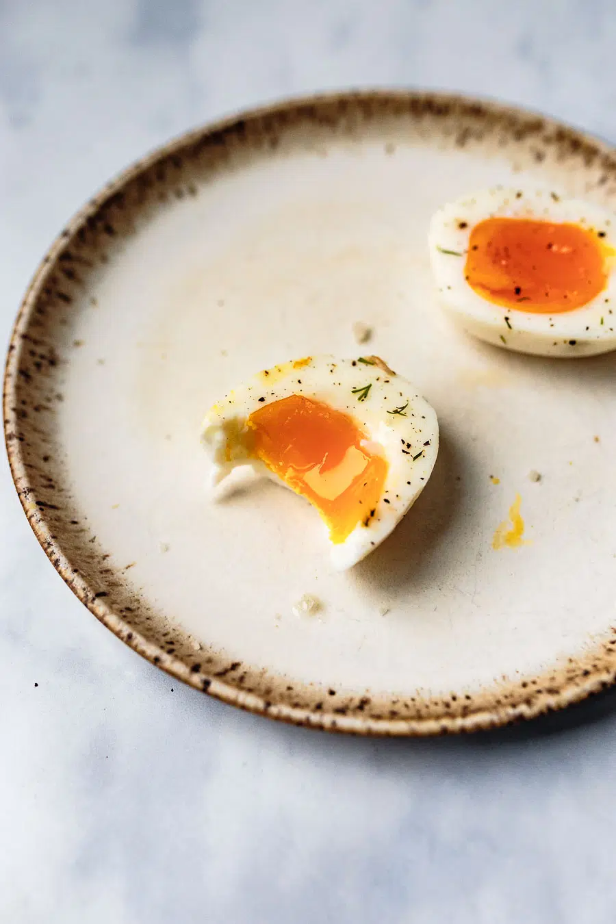 three jammy boiled eggs halved and resting on a stoneware place topped with salt and pepper and a bite taken out of one of them