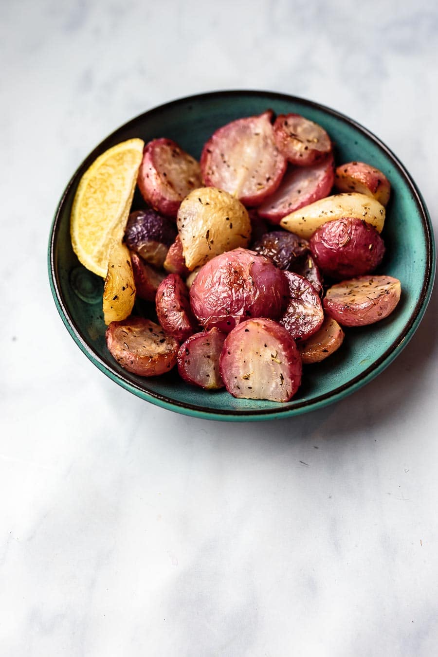 a teal bowl full of roasted radishes with a lemon wedge