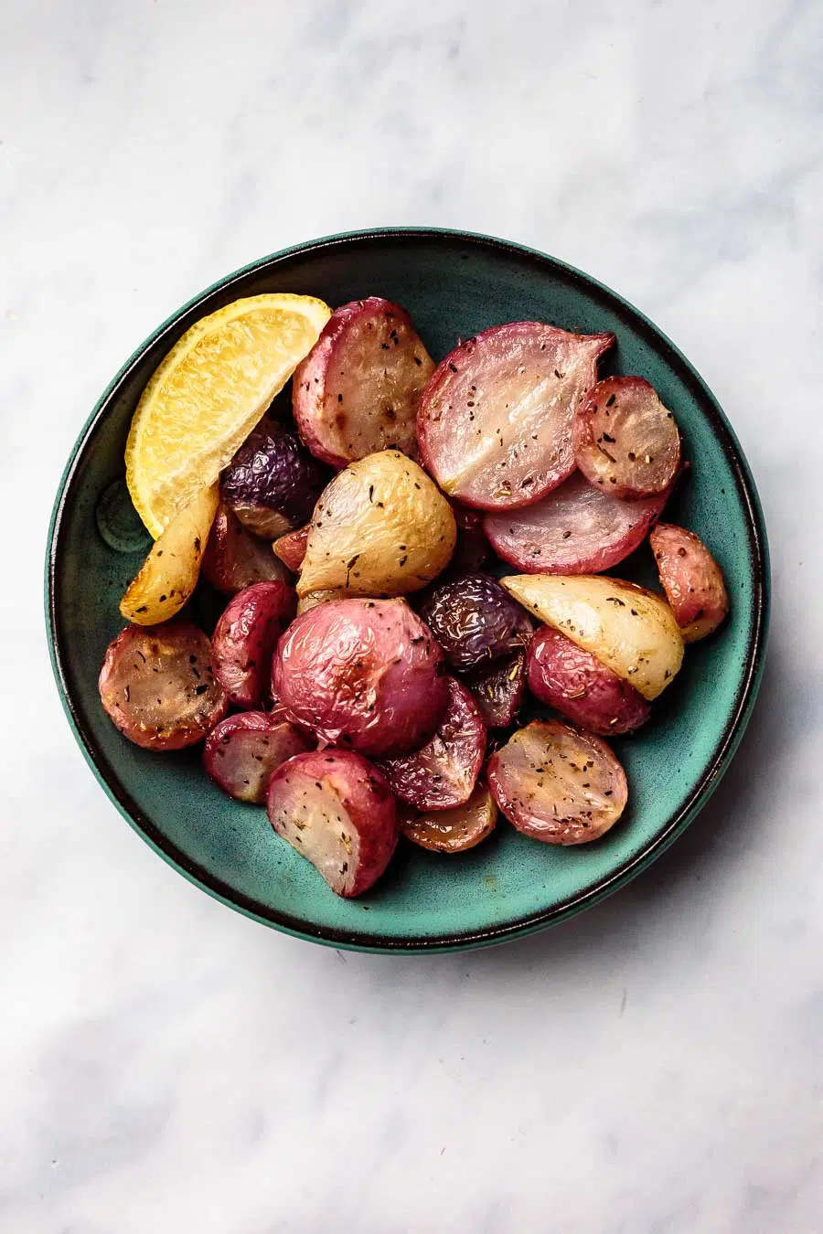 a teal bowl full of roasted radishes with a lemon wedge
