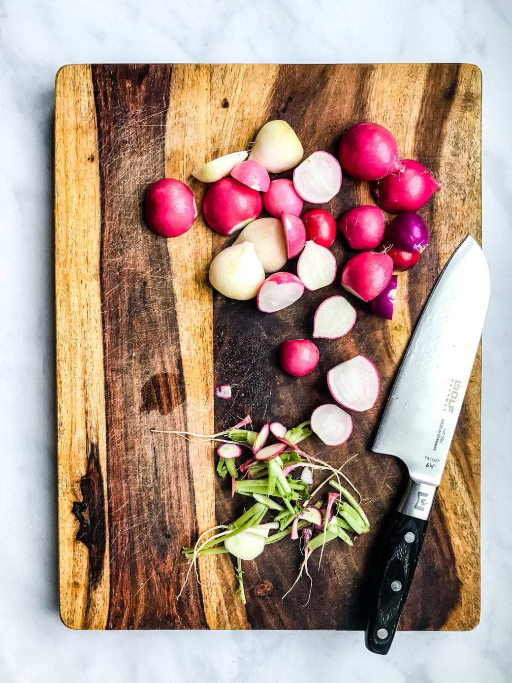 fresh radishes that have had their tops and bottoms trimmed resting on a wooden cutting board with a sharp kitchen knife