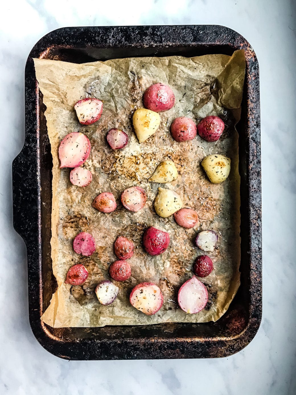 radishes that have been sliced in half and roasted in olive oil, salt, and dried rosemary resting on a prepared baking sheet