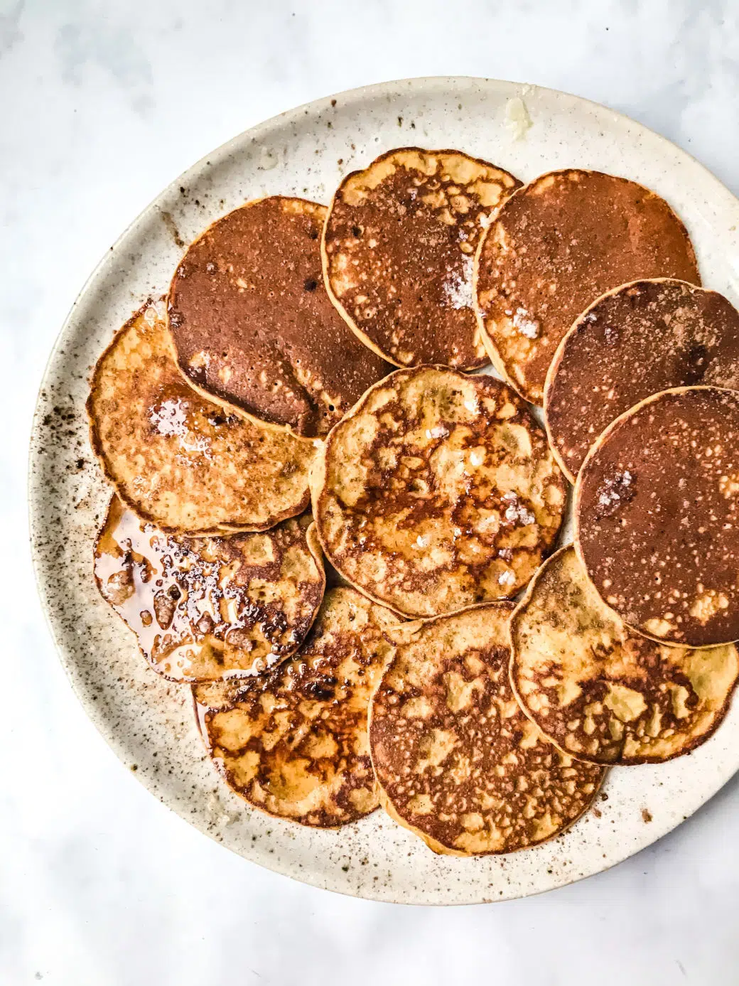 several Paleo Sweet Potato Silver Dollar Pancakes on a stoneware plate topped with melted ghee and cinnamon