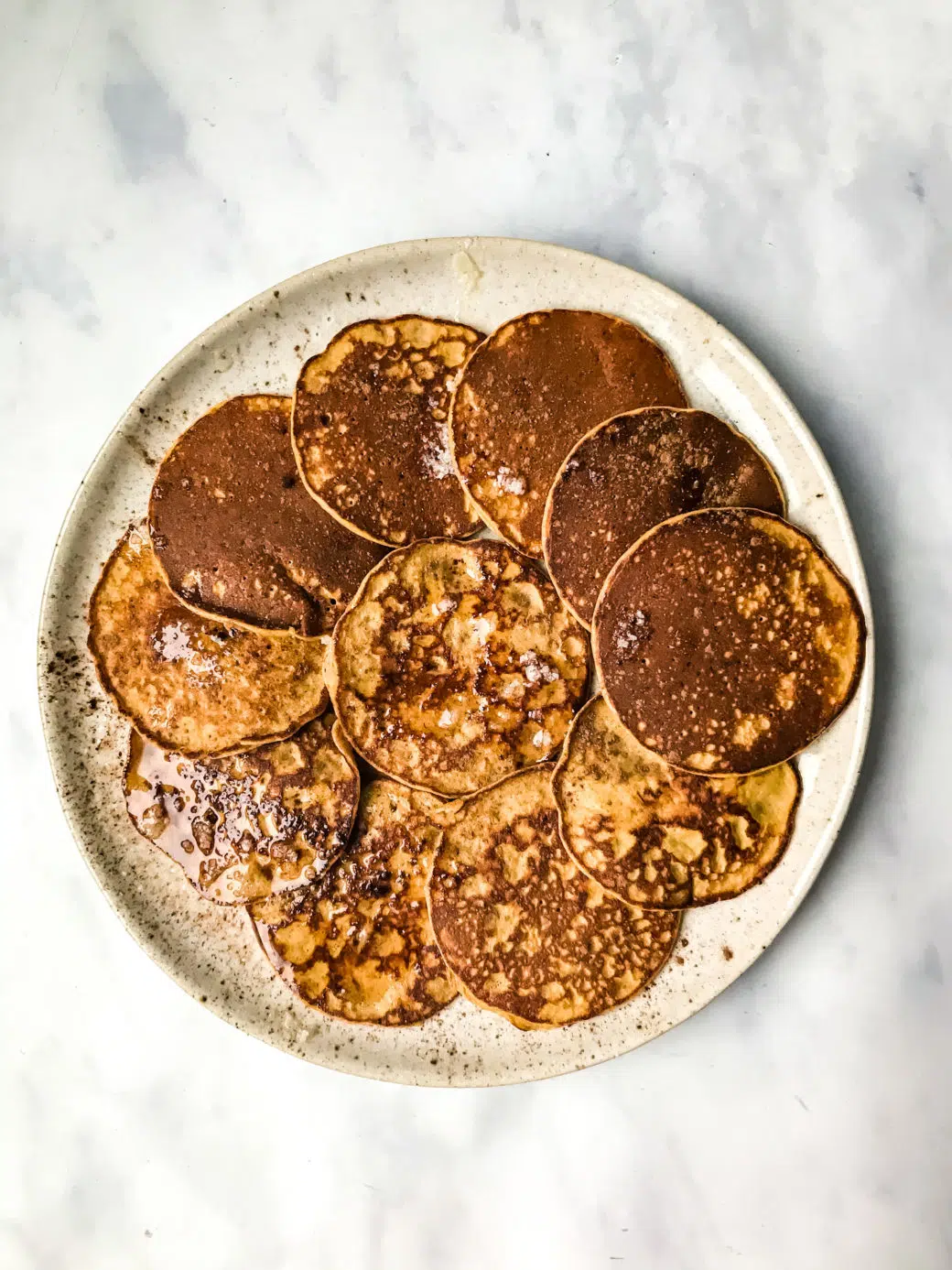 several Paleo Sweet Potato Silver Dollar Pancakes on a stoneware plate topped with melted ghee and cinnamon