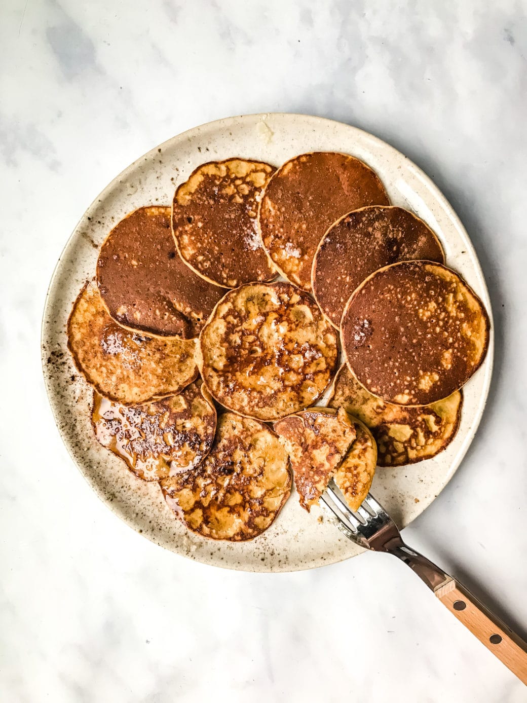 several Paleo Sweet Potato Silver Dollar Pancakes on a stoneware plate topped with melted ghee and cinnamon with a fork