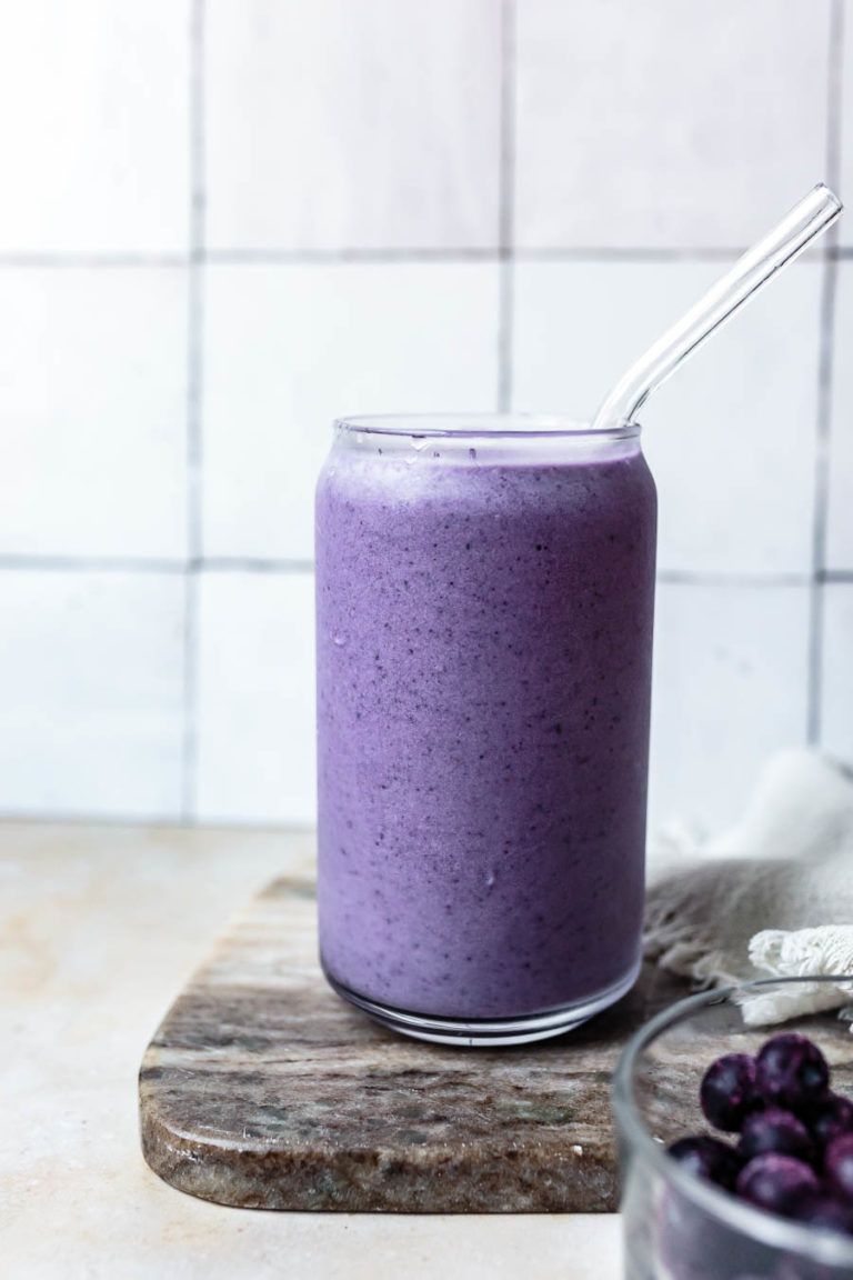 Glass with purple blueberry bone broth smoothie in it, sitting on a wooden chopping board.