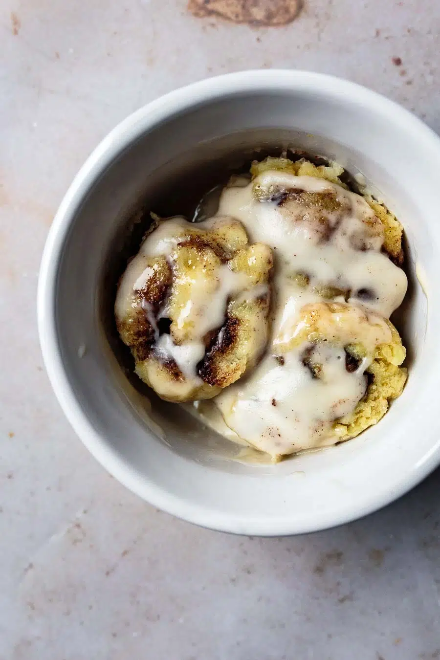 3 small pieces of this cinnamon roll sitting in a white bowl on a light colored counter top. They have been topped with a cream colored date sauce.