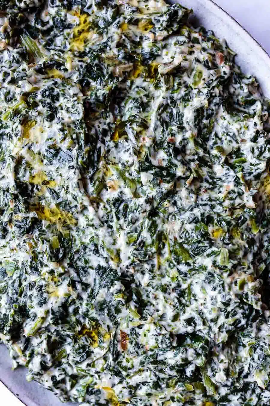 Close up of vegan creamed spinach. Only part of the edge of the plate is visible on the right. The dish is very green with a white sauce throughout it.