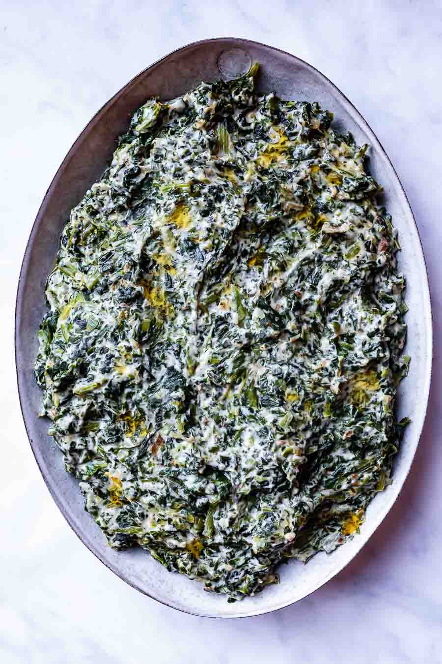 View form above of creamed spinach with coconut milk on a large grey oval serving plate. It is very green with a white sauce throughout. The plate is on a white counter.
